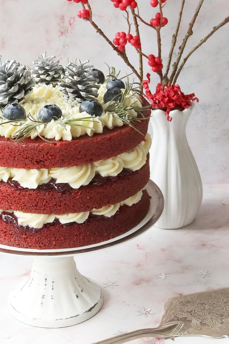 Elegant red velvet cake with blueberries, cream, and decorative pine cones.
